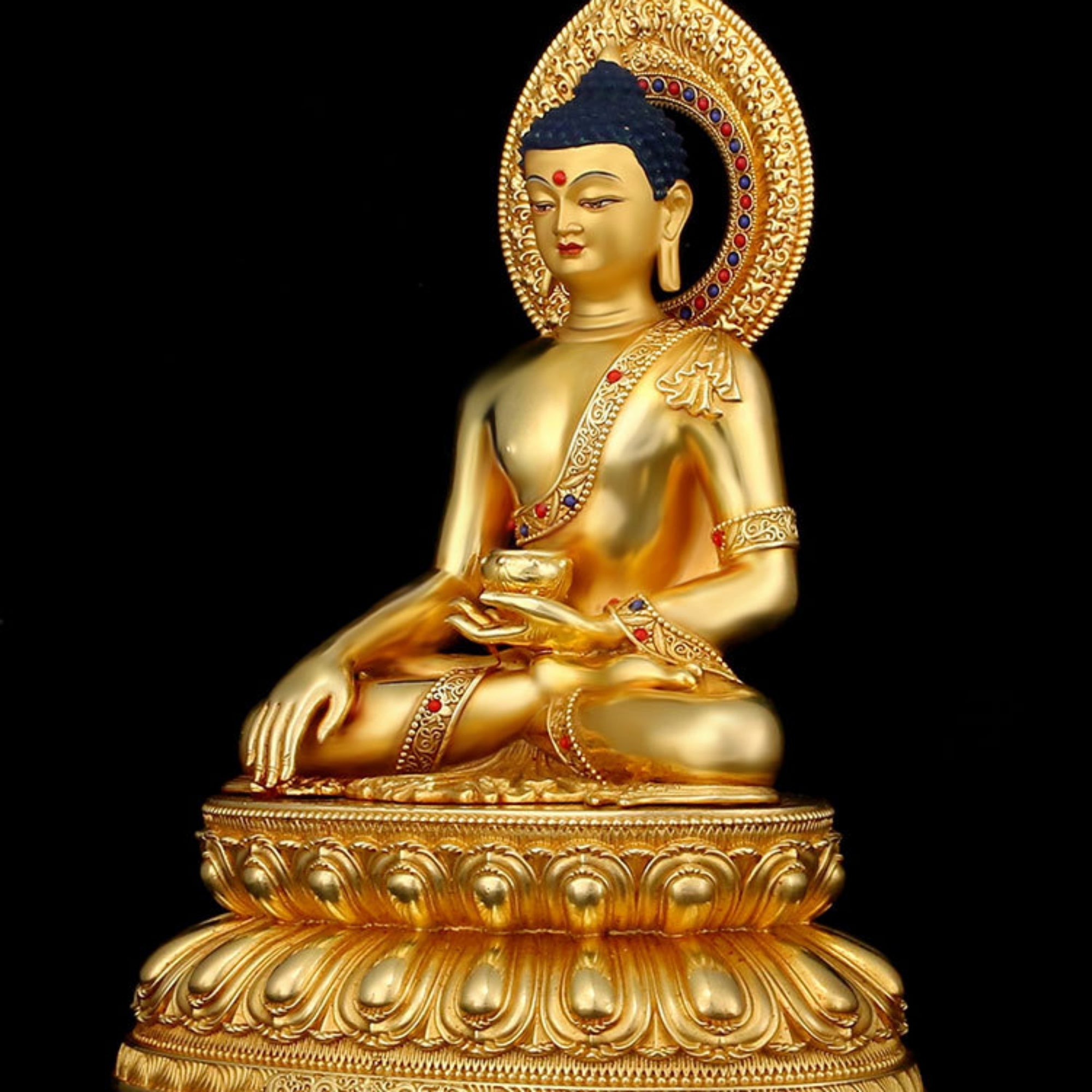 A golden Buddha statue seated in a meditative pose on a lotus base, photographed against a solid black background.