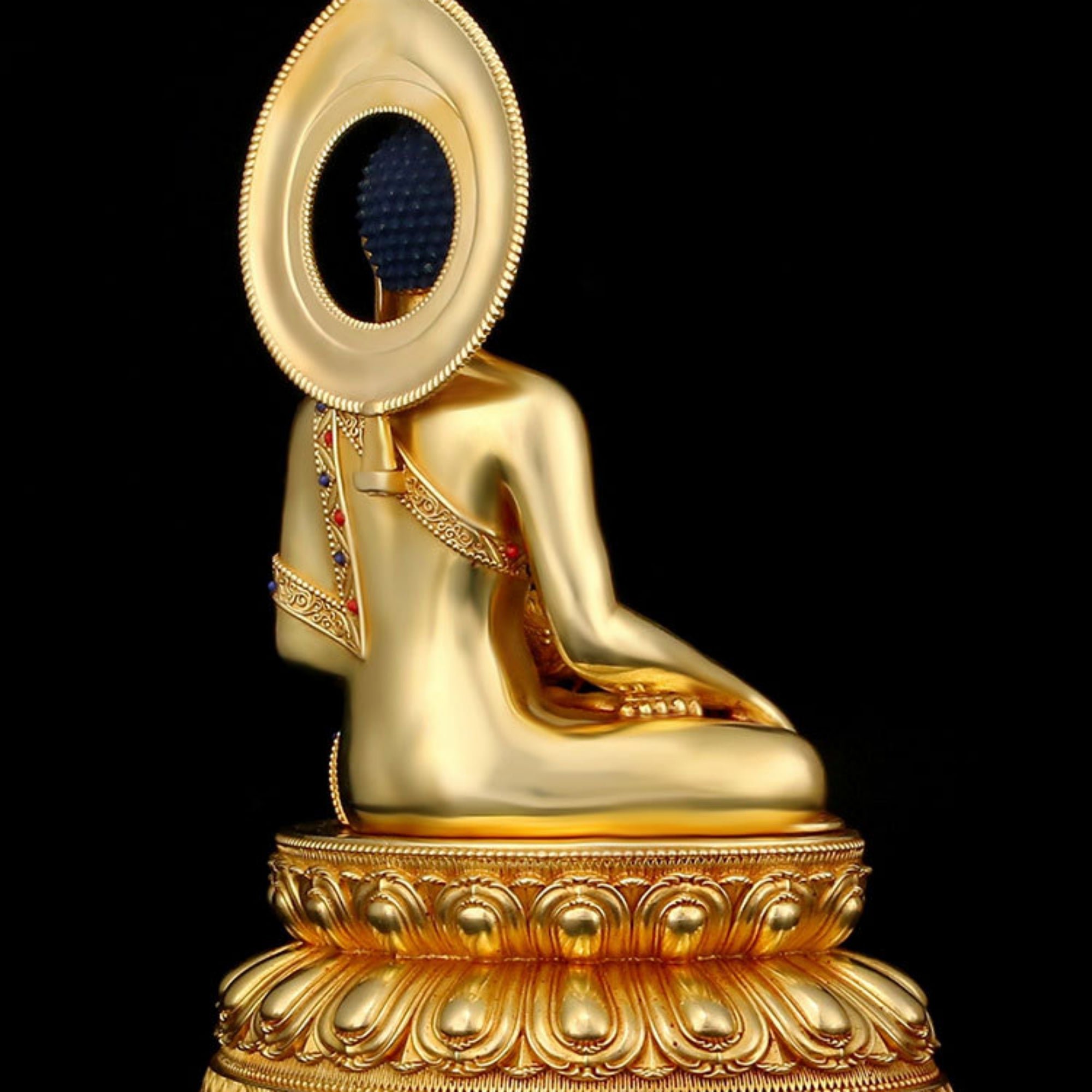 A golden Buddha statue shown from the back, seated on an ornate lotus-style base against a solid black background.