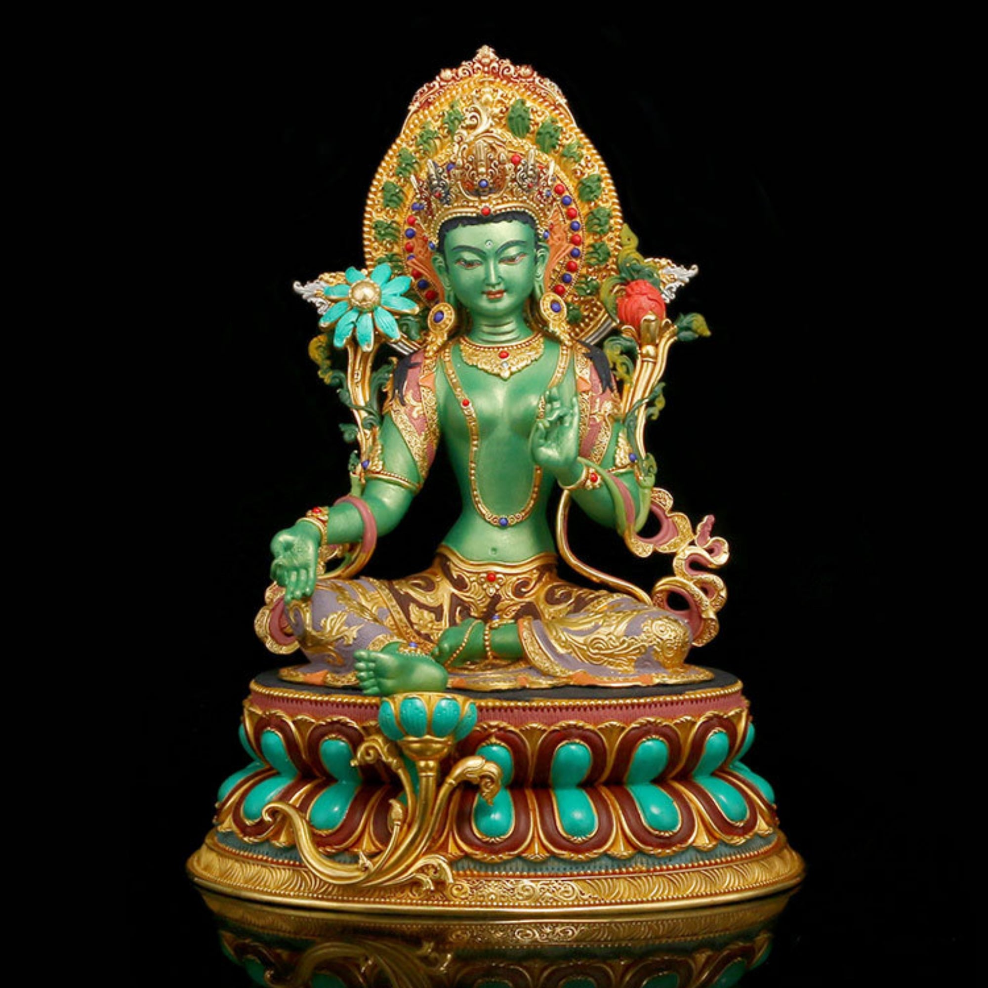 A green and gold seated deity statue with turquoise accents, ornate jewelry, and a decorative lotus base, photographed against a solid black background.