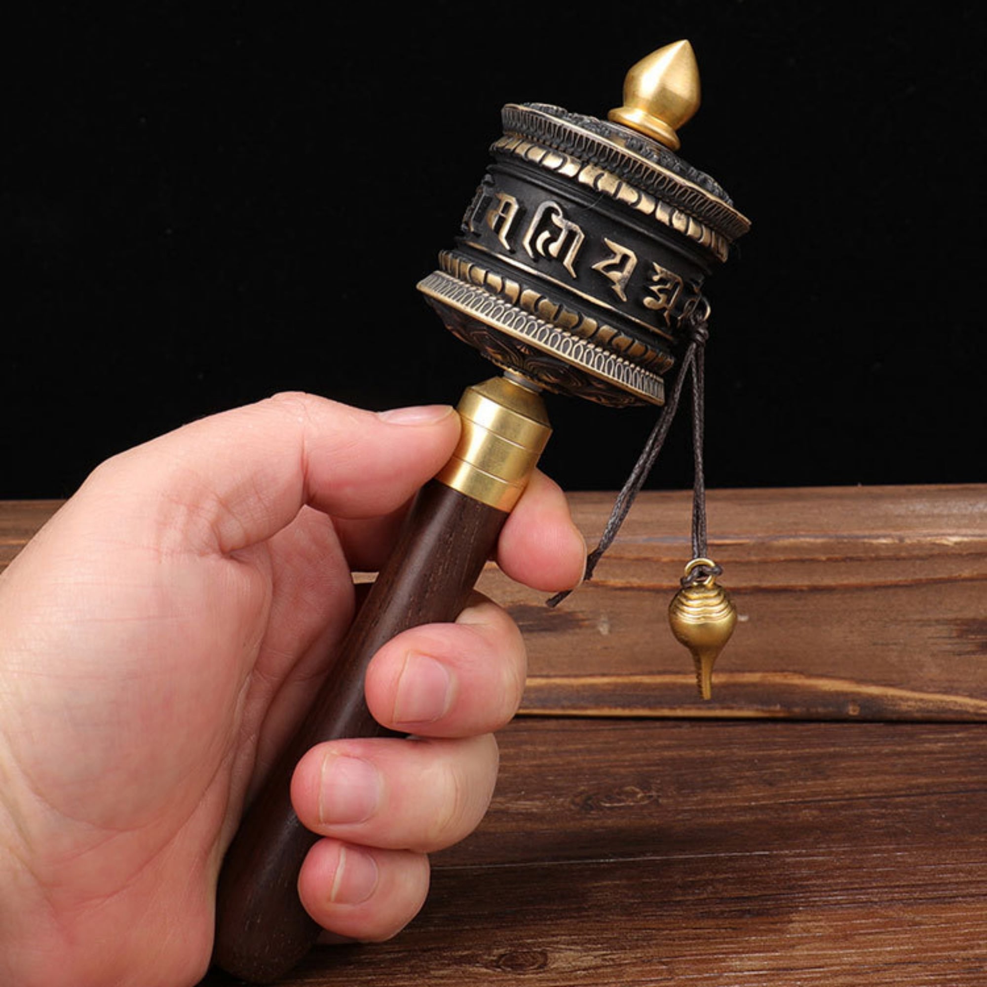 Hand holding a traditional prayer wheel against a dark background