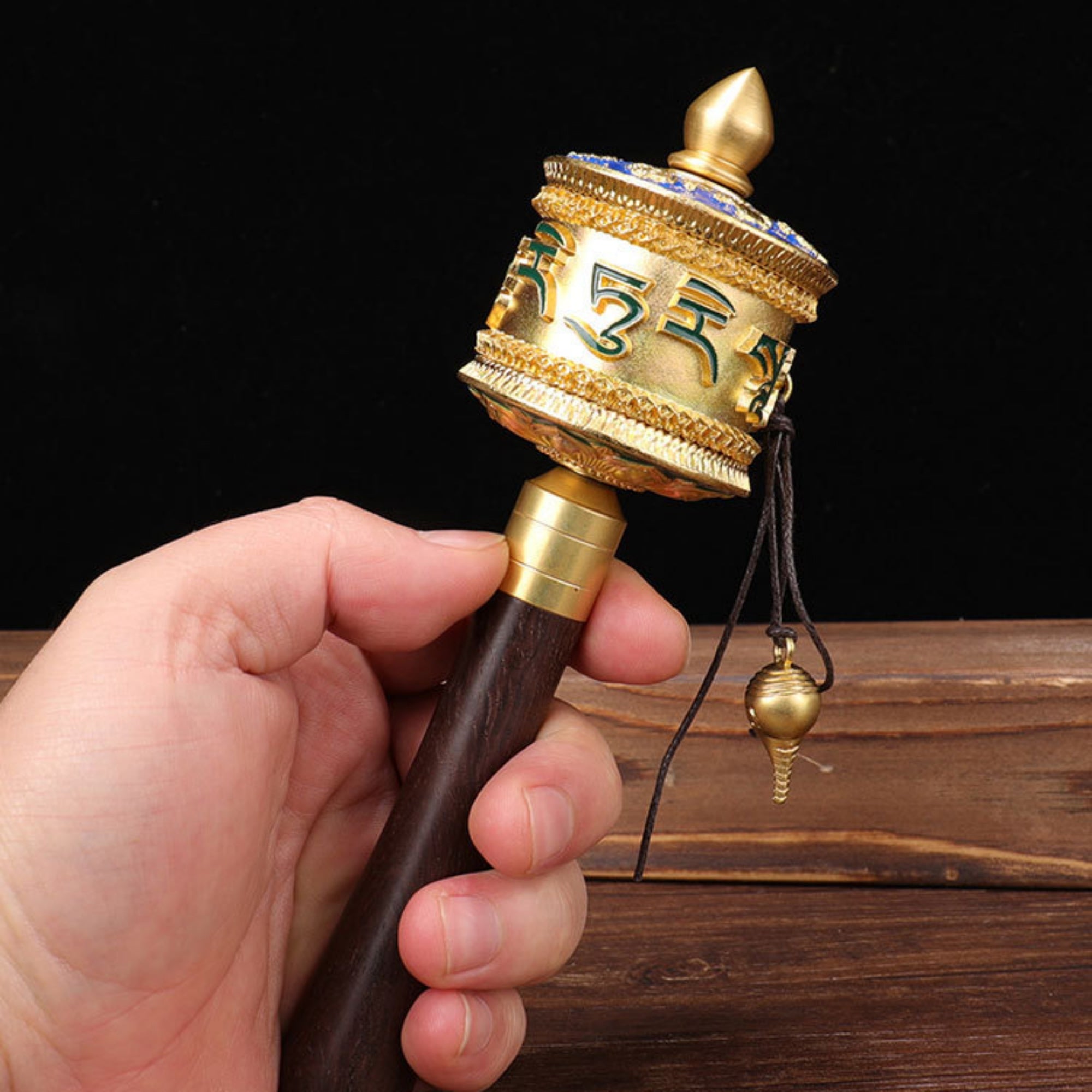 Hand holding a gold and brown prayer wheel against a dark background