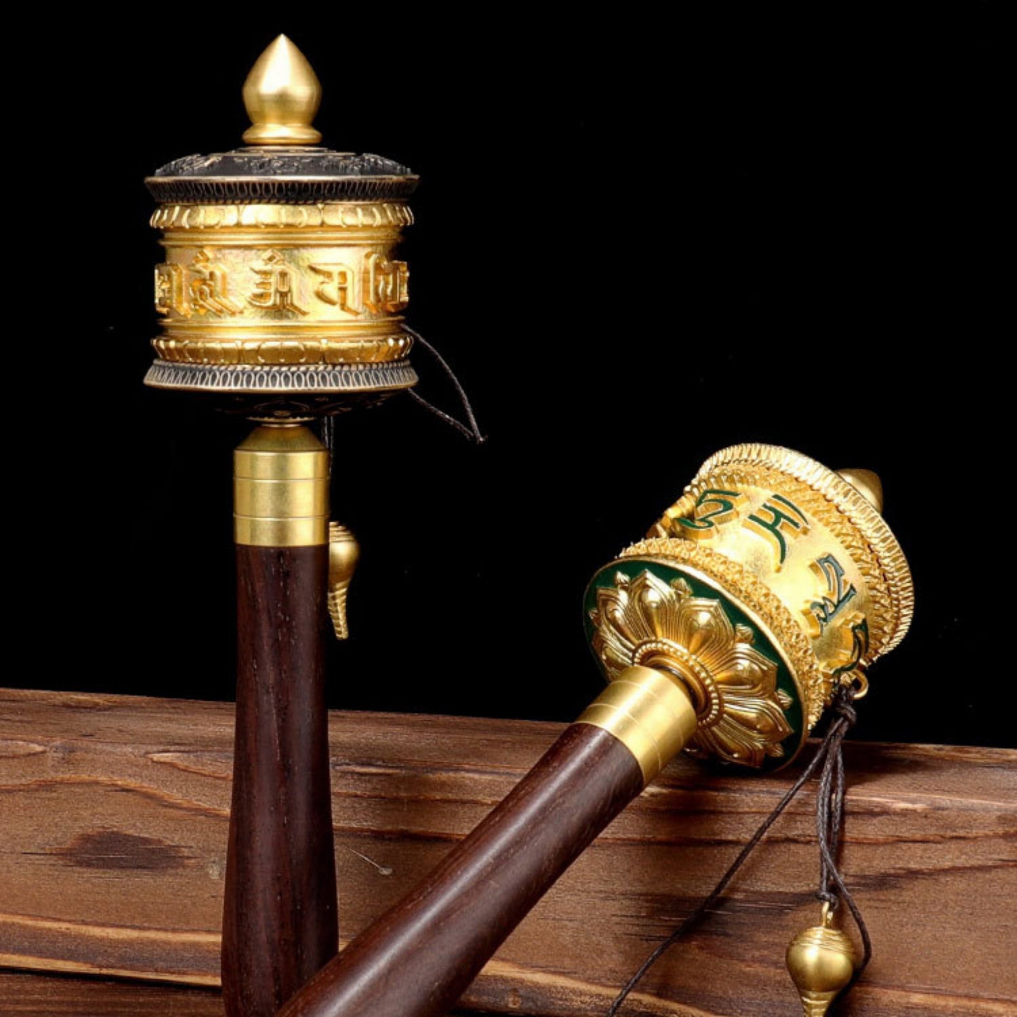 Two ornate prayer wheels on a wooden surface with a black background