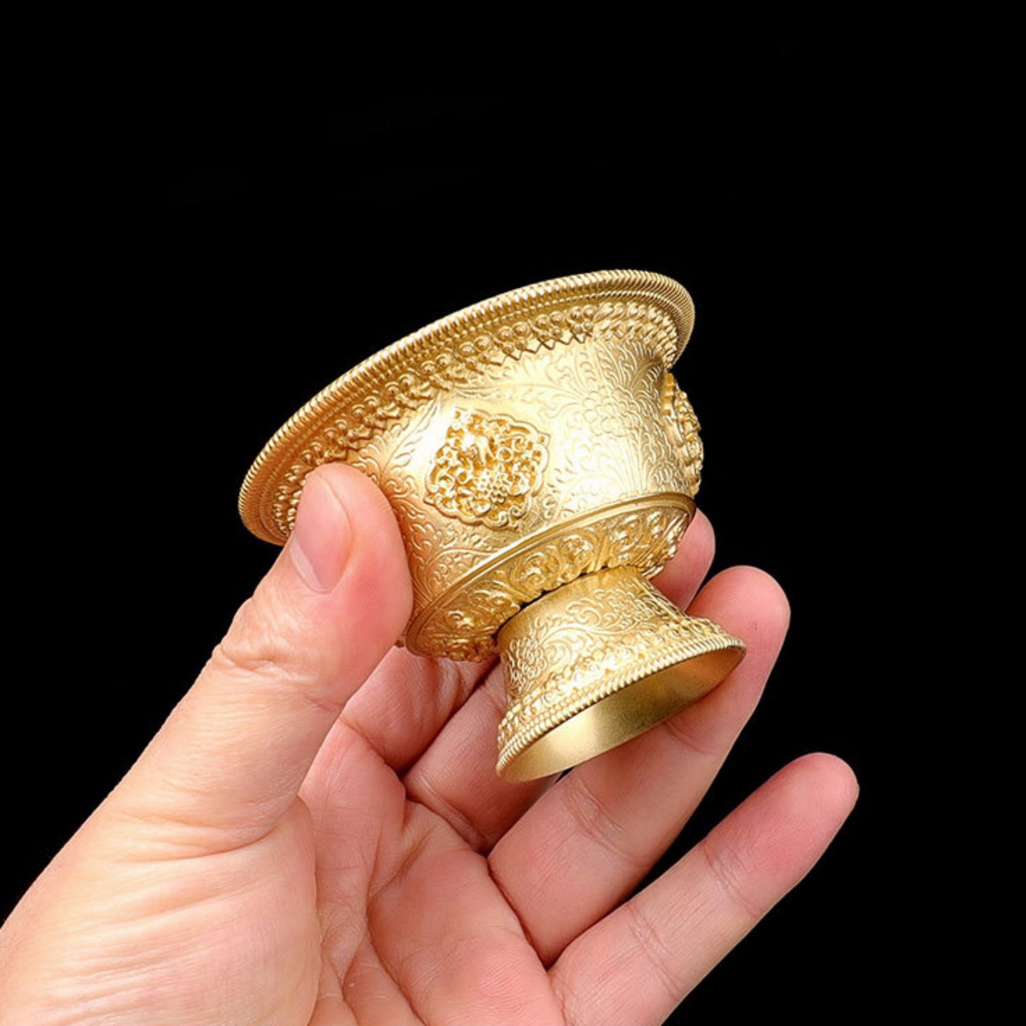 Gold ornate cup held in a hand against a black background