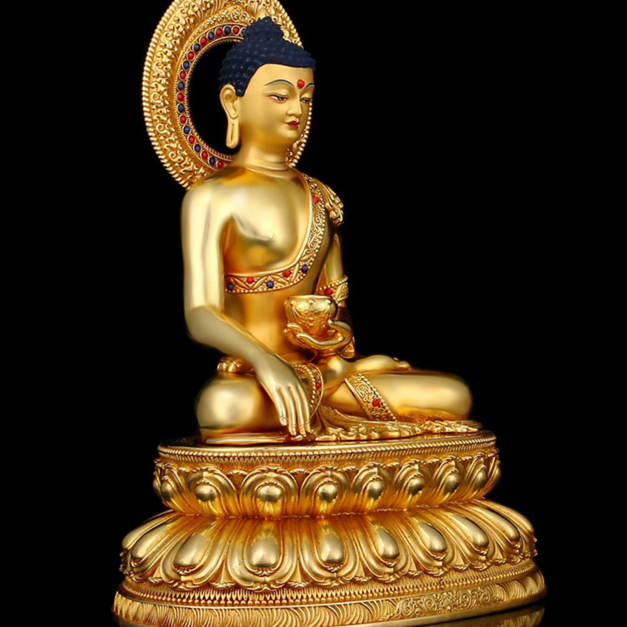 A golden Buddha statue seated in a meditative pose on an ornate lotus base, photographed against a solid black background.