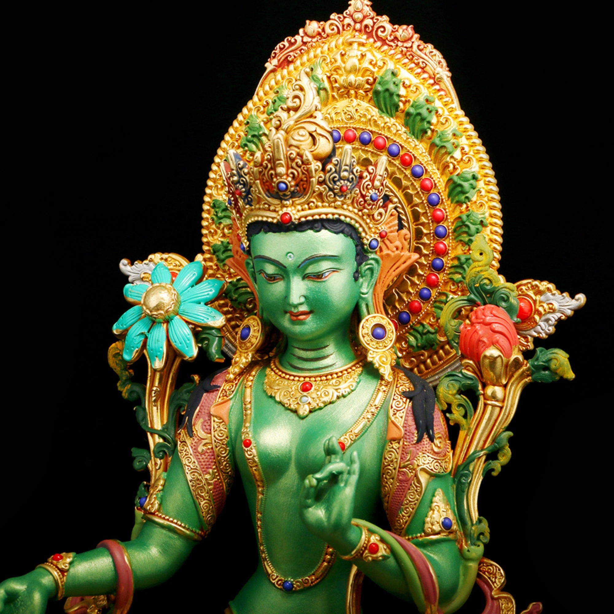 A detailed green and gold statue of a deity with ornate jewelry, a large jeweled headdress, and floral motifs, set against a solid black background.