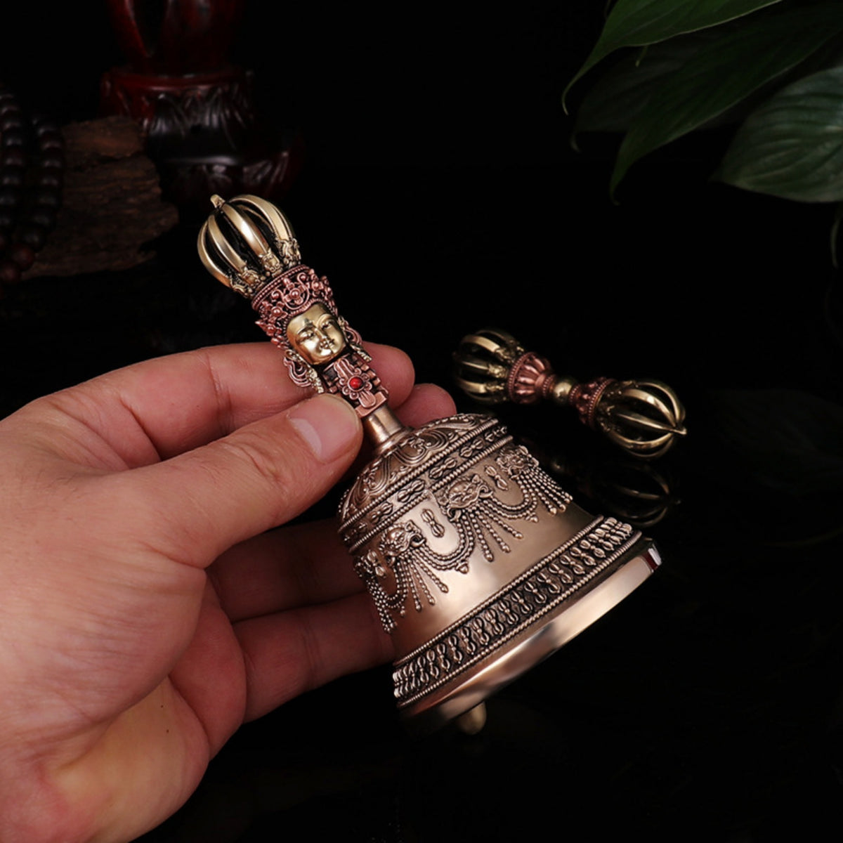 Hand holding a ornate brass bell with intricate designs against a dark background