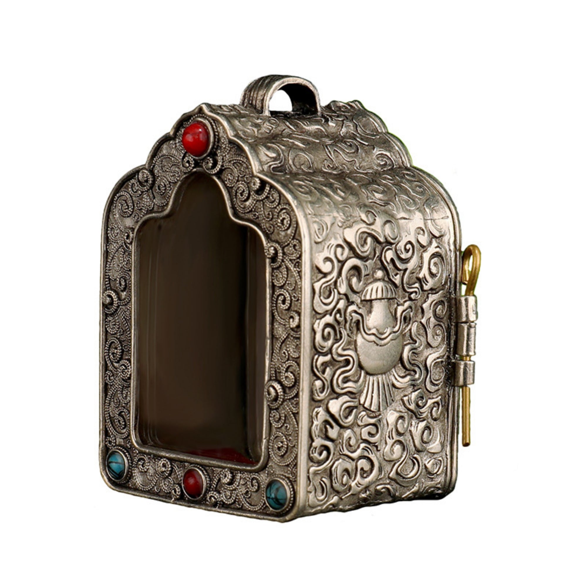 An ornate silver-toned metal keepsake box with intricate embossed scrollwork, a central recessed window, decorative red and blue gemstones, and a small gold key attached to the side, shown on a plain white background.