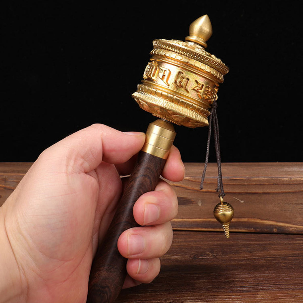 Hand holding a gold and brown prayer wheel against a dark background