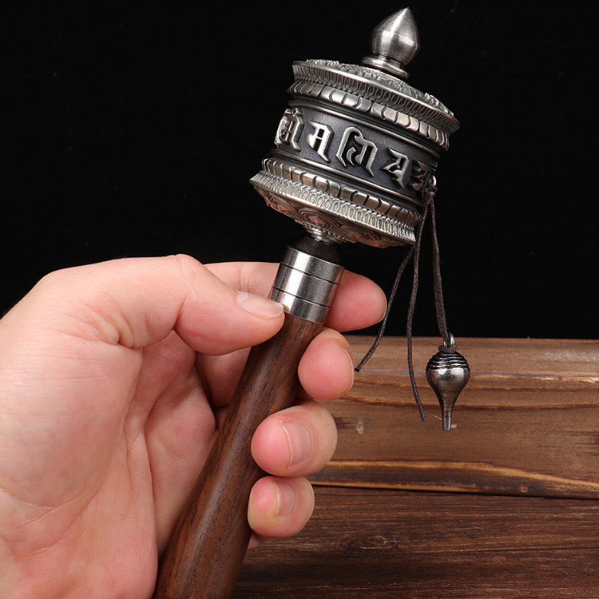Hand holding a traditional metal and wooden prayer wheel against a dark background