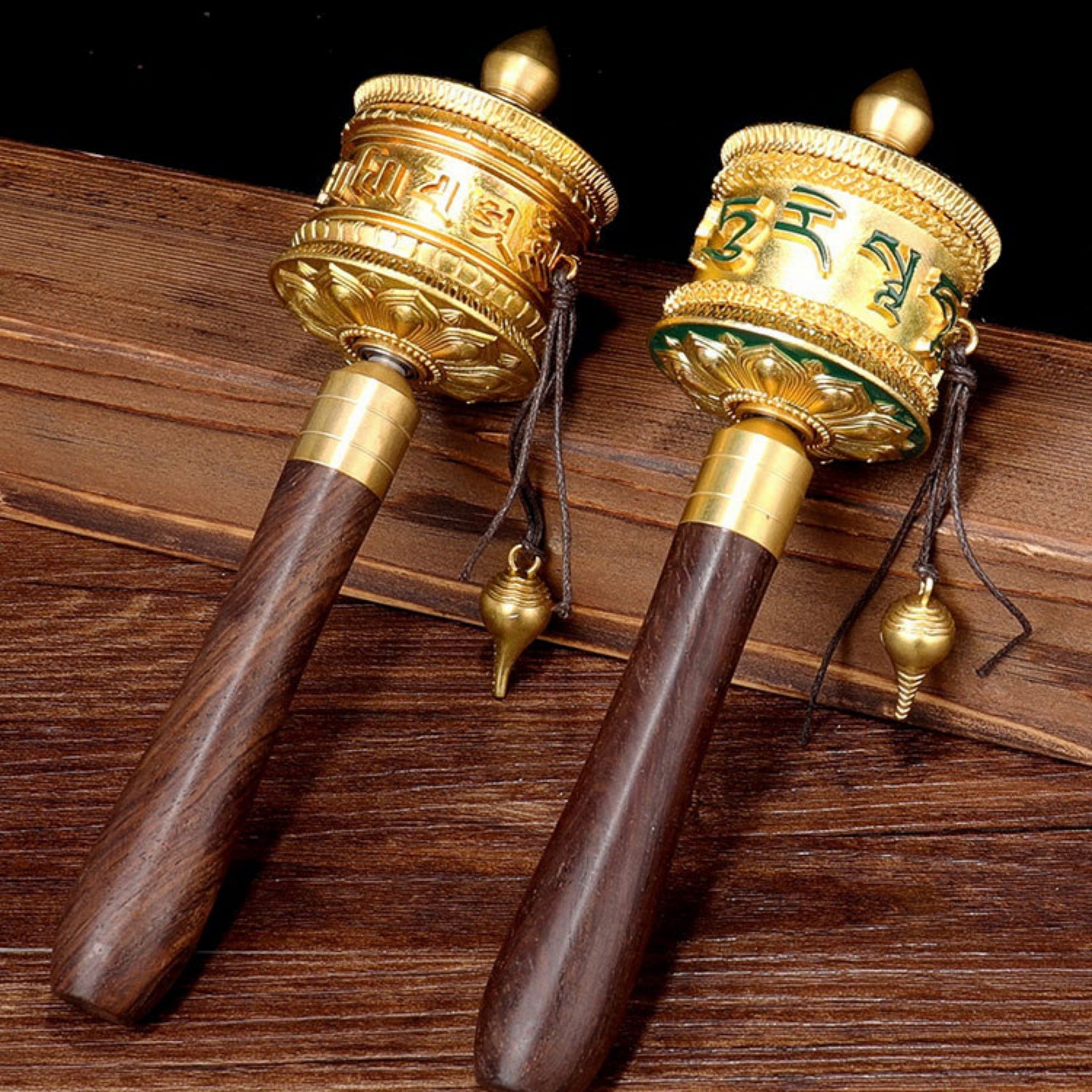 Two prayer wheels with gold accents on a wooden surface