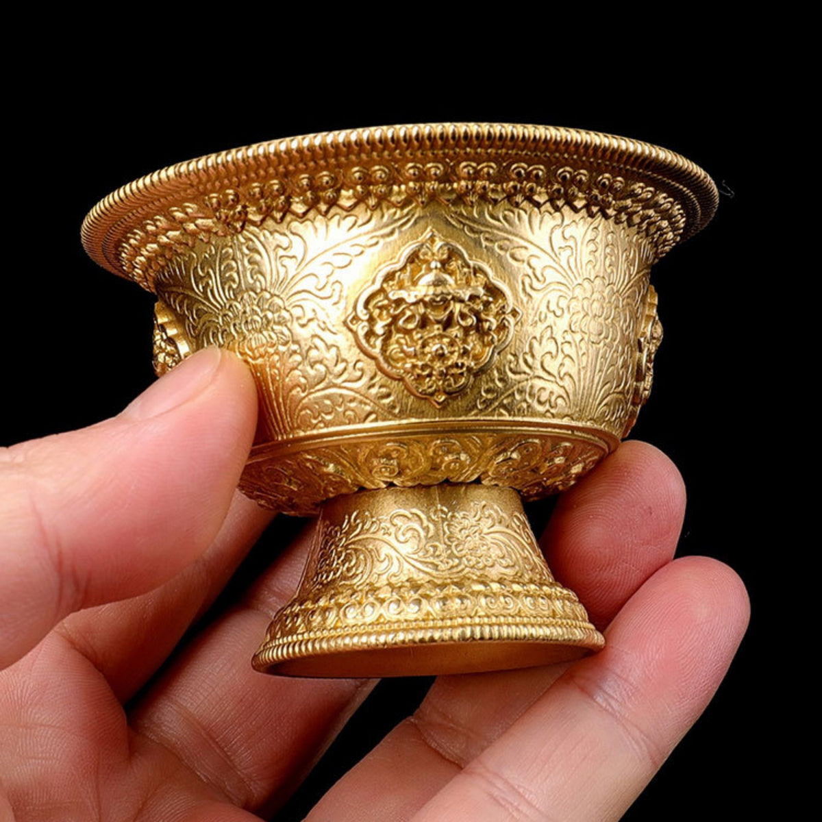 Hand holding a gold ornate cup against a black background