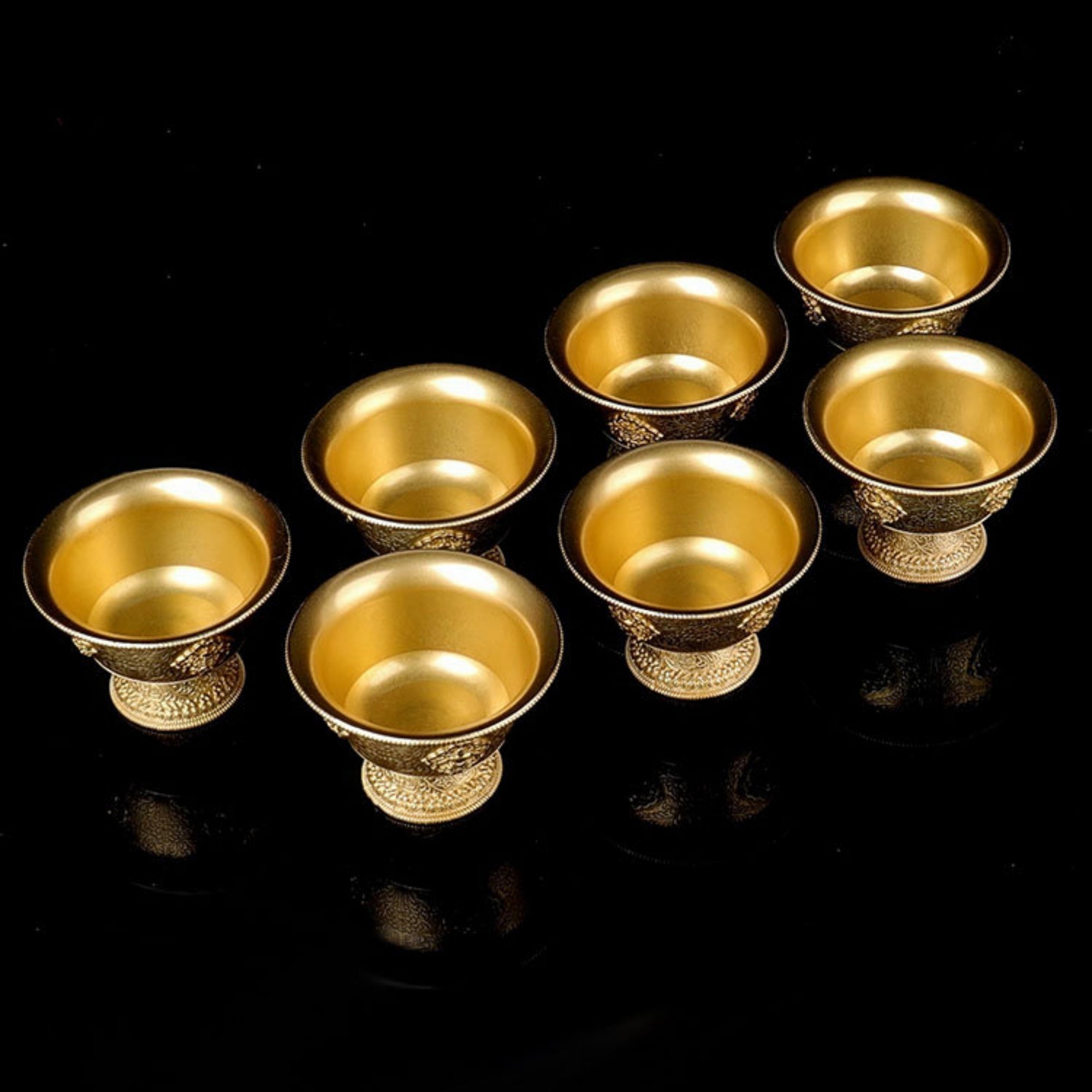 Set of eight gold cups with intricate designs on a black background