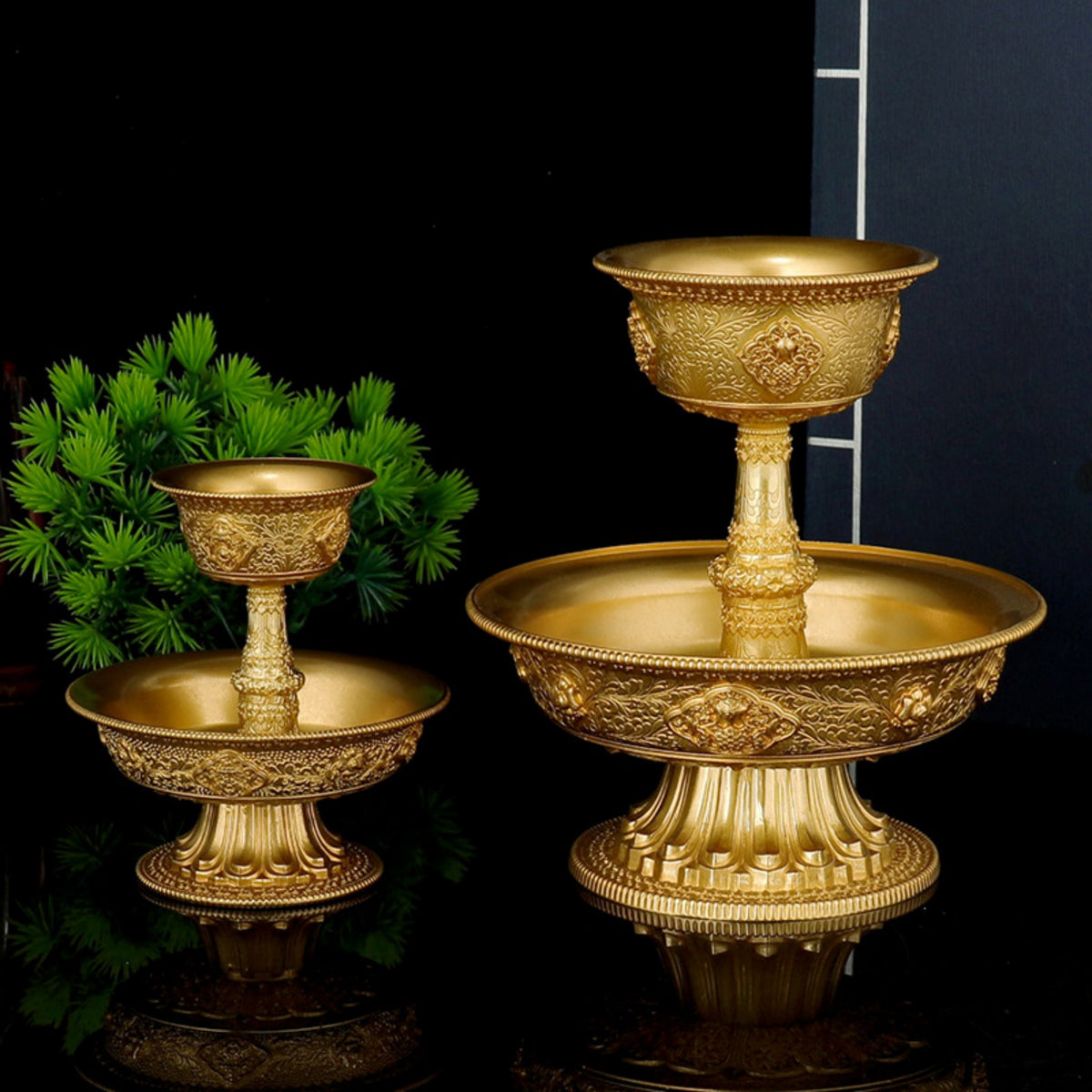 Set of three ornate gold candle holders on a reflective surface with a dark background.