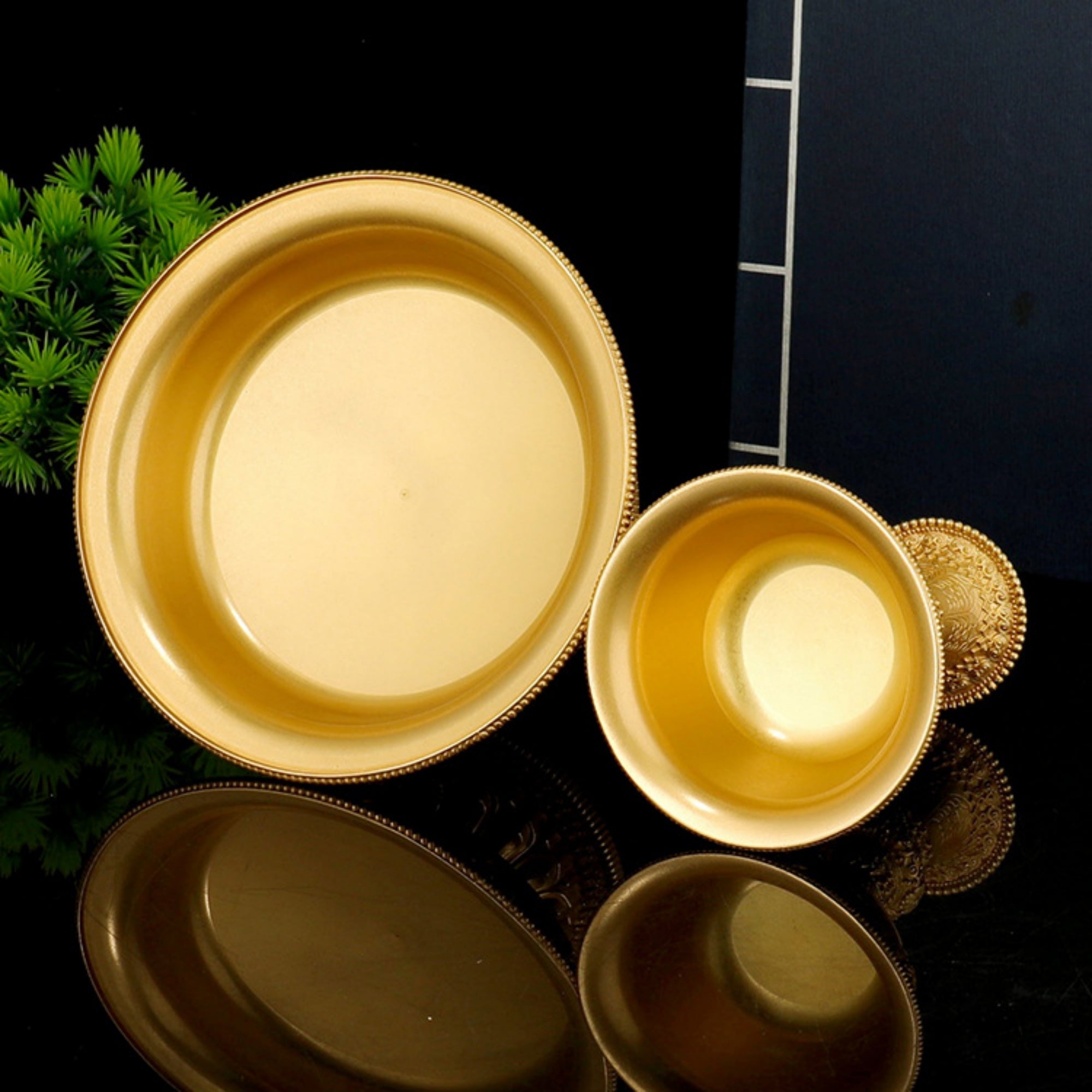 Set of gold ceramic plates on a black surface with greenery in the background