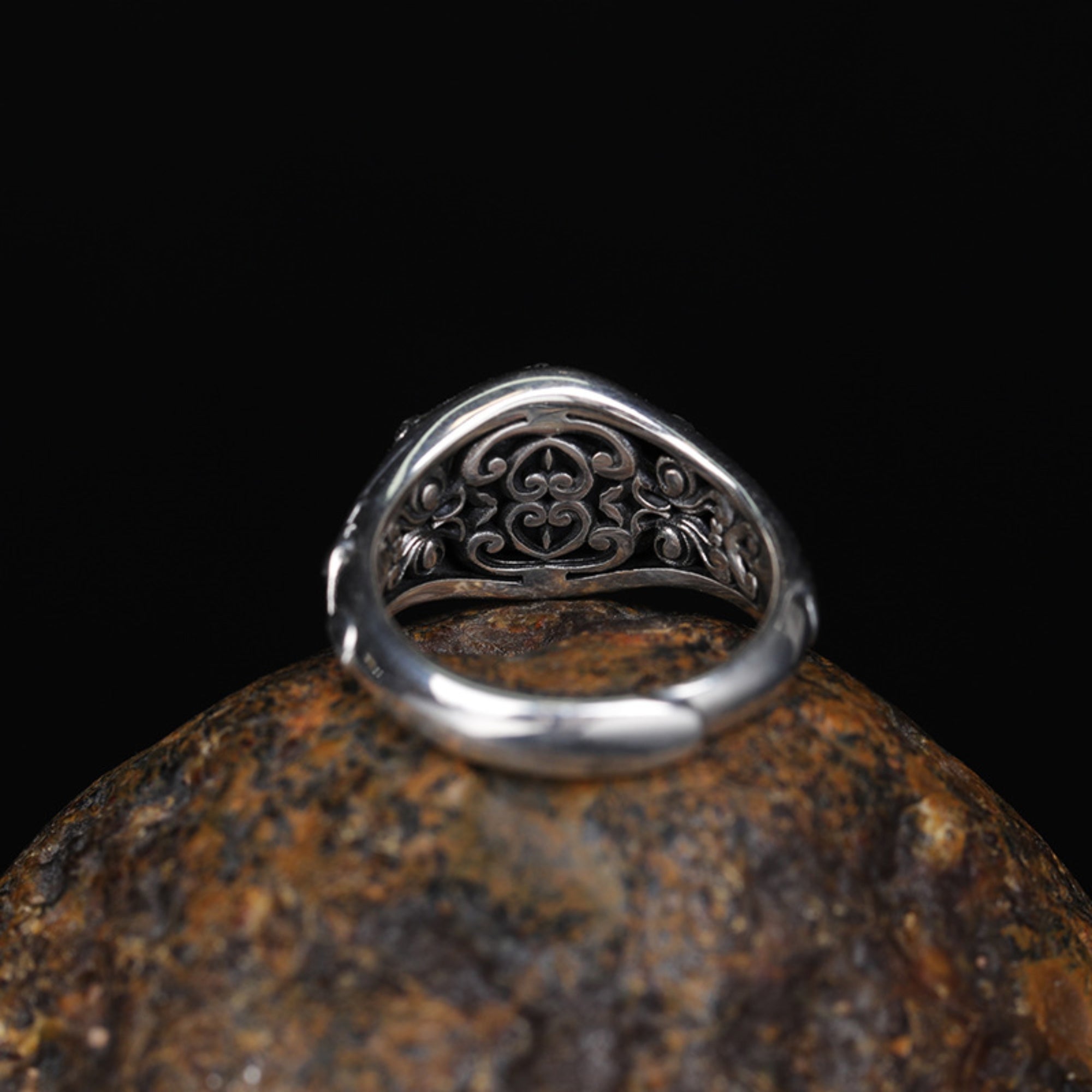 Silver ring with intricate design on a textured stone surface