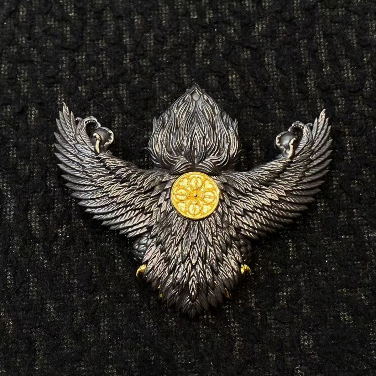 Decorative brooch with wings and a gold center on a black textured background