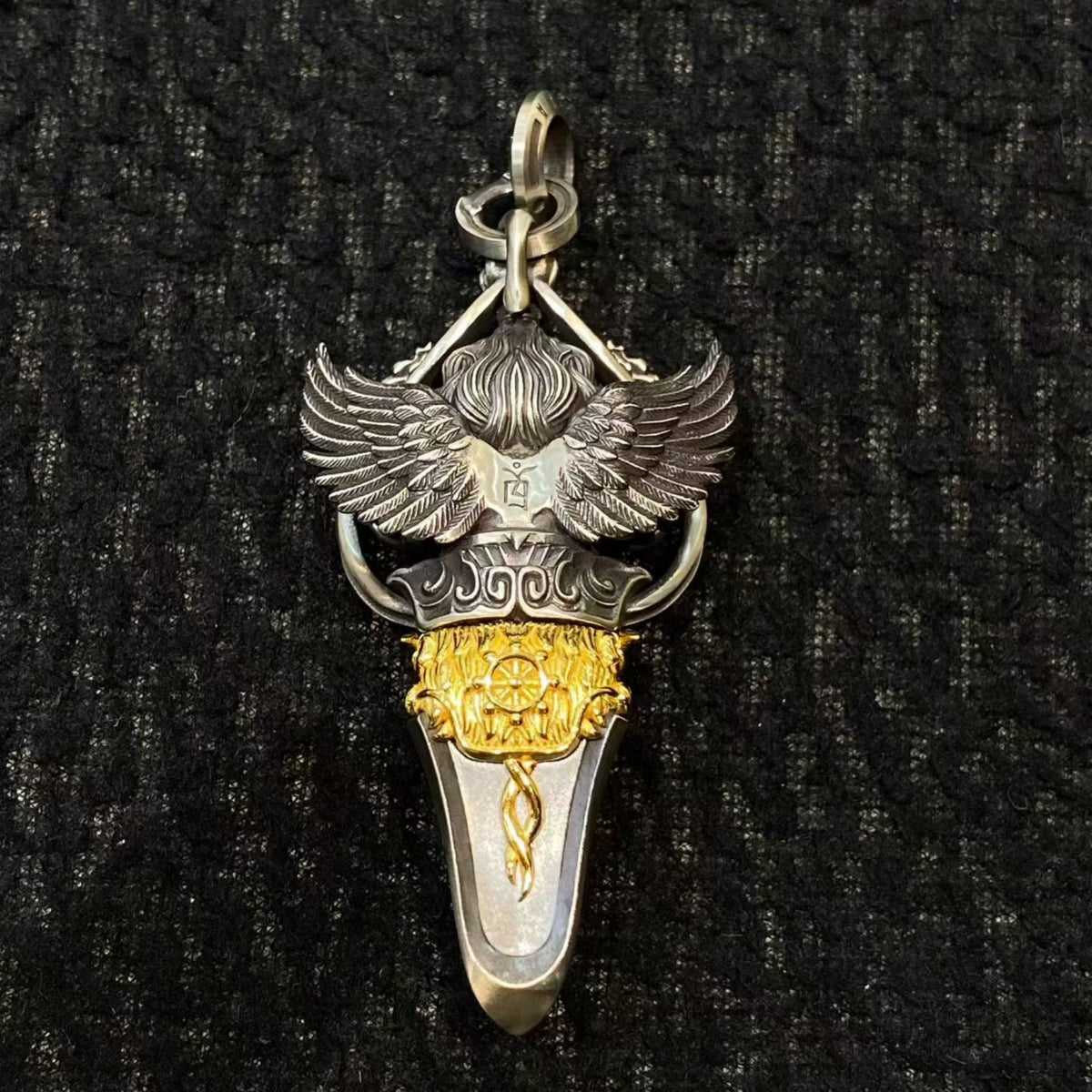 Silver and gold pendant with wings on a black textured background