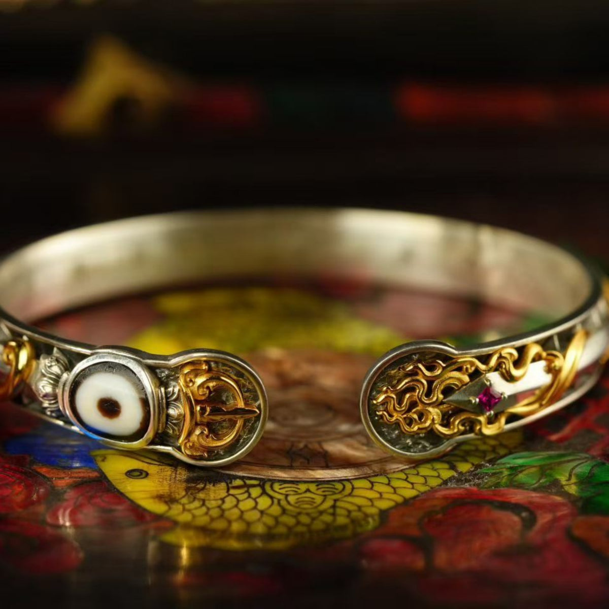 Gold and silver bracelet with intricate designs on a colorful surface