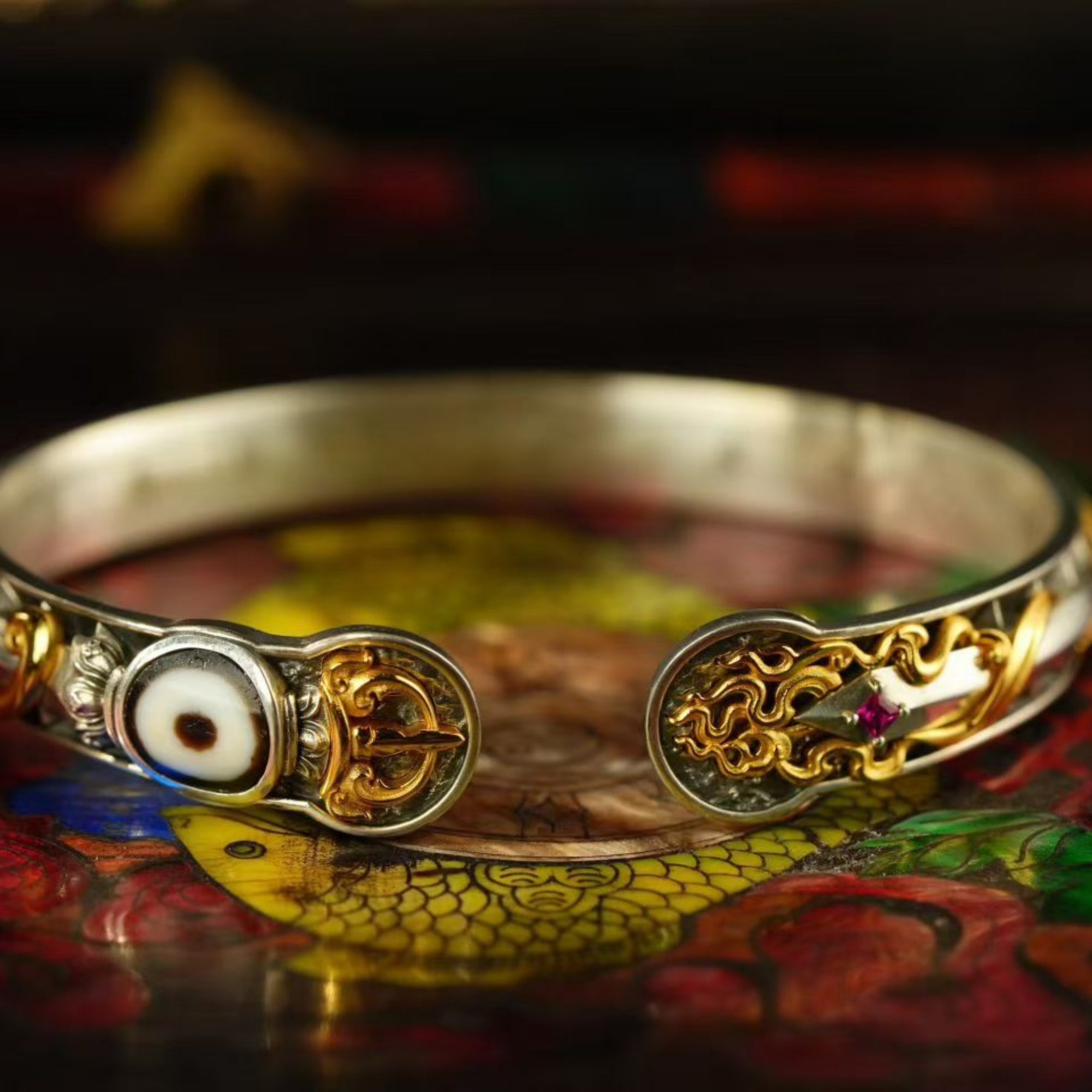 Gold and silver bracelet with intricate designs on a colorful surface