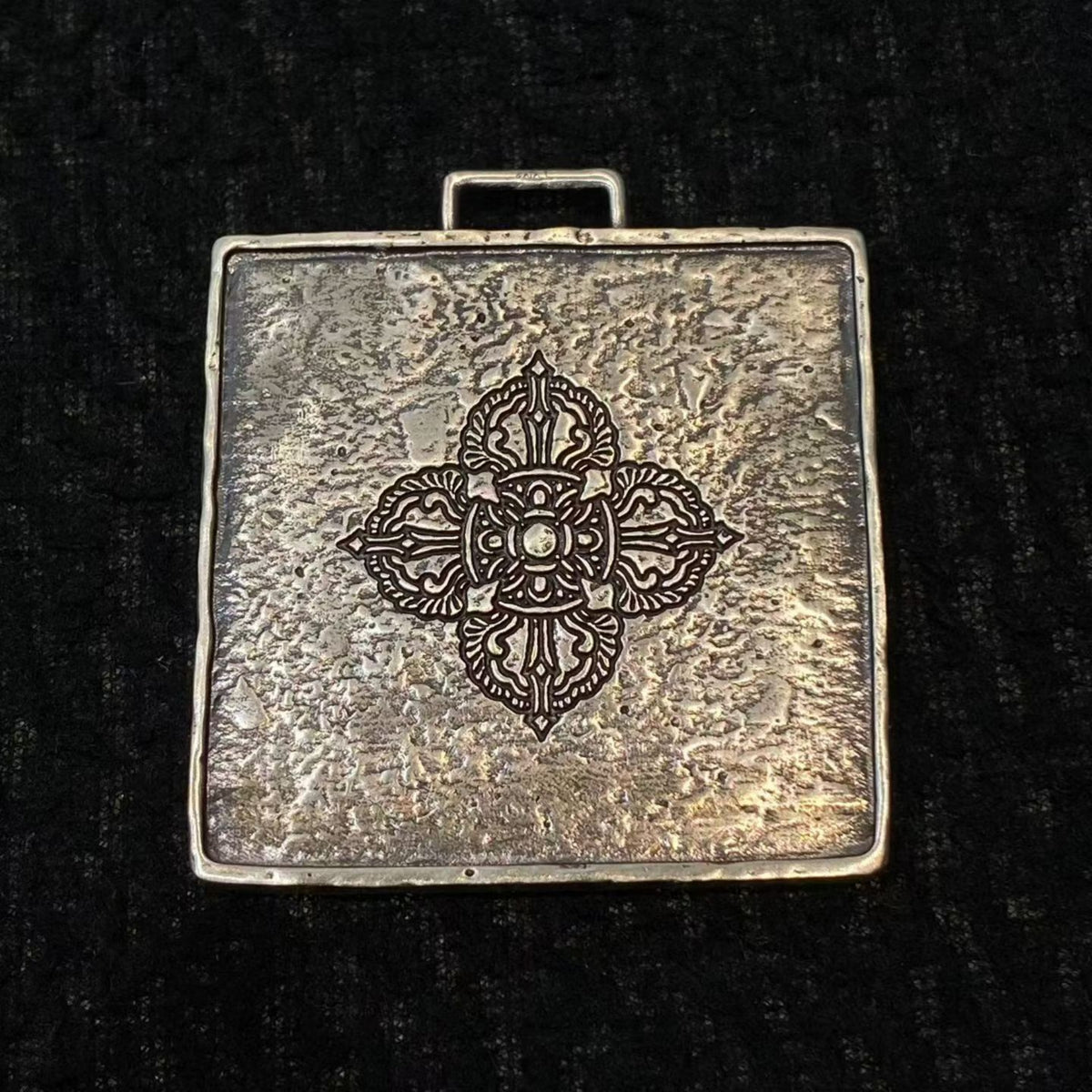 Decorative silver pendant with intricate design on a black background