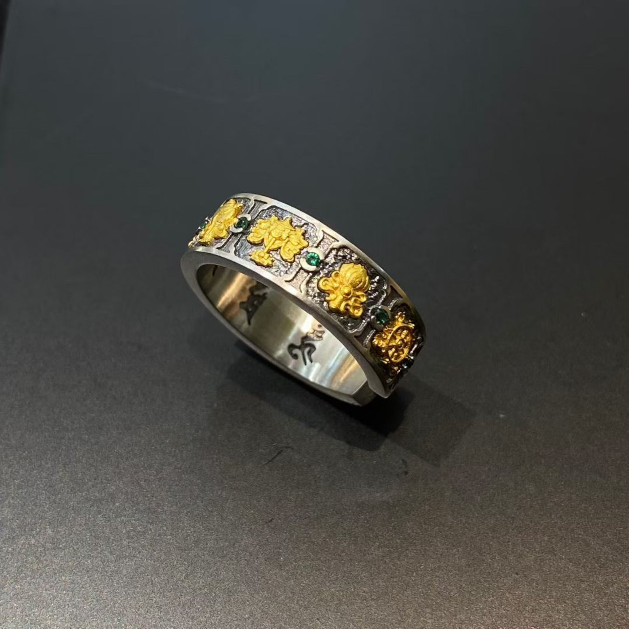 Silver ring with gold floral designs on a dark gray background